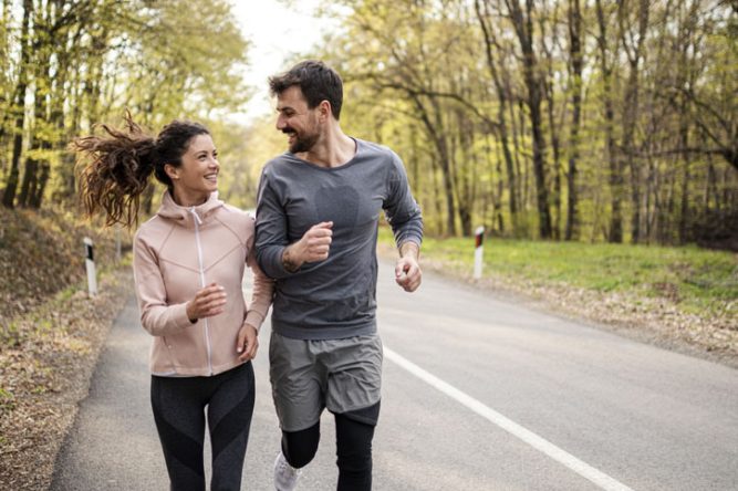 Jeune couple courant sur une route en forêt